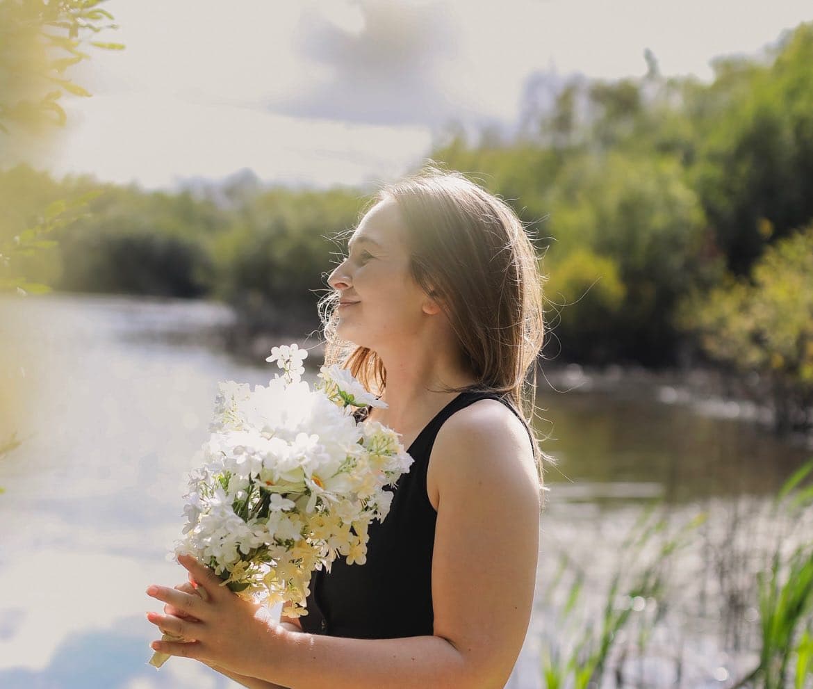 Rebecca holding white flowers beside a peaceful lake